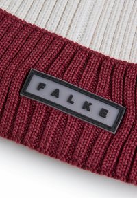 Dziana czapka z prążkowanym bordowym wzorem i kremowym paskiem; posiada czarną prostokątną naszywkę z białymi literami "FALKE".