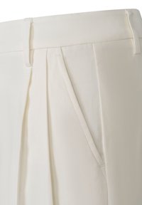 Gros plan d’un pantalon blanc sur mesure montrant des passants de ceinture, des plis et une poche latérale inclinée.
