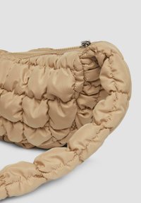 Beige gepolsterte Handtasche mit einem strukturierten, gesteppten Design, ausgestattet mit einem Reißverschluss und einem geflochtenen Tragegriff, hergestellt aus glattem, glänzendem Stoff.