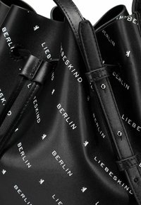 Borsa a secchiello in pelle nera con testo stampato bianco "LIEBESKIND BERLIN" e icona di leone. Texture liscia, cinture strette e design morbido.