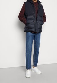 Laivastonsininen toppaliivi hupulla, päällä punaruudullinen paita, yhdistettynä sinisiin farkkuihin ja valkoisiin tennareihin. Sisältää vetoketjusuljetuksen ja sivutaskut.