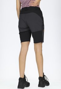 Svart och grå vandringsshorts med cargoficka, elastisk midja och knälång design, tillsammans med svarta friluftsskor.
