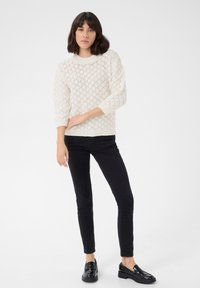 Pull en tricot crème avec un motif en losanges, poignets et bas côtelés. Assorti avec un jean skinny noir et des loafers noirs brillants.