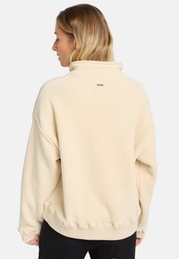 Romige fleece pullover met een hoge kraag, geribbelde textuur en elastische zoom. Bevat een klein logo nabij de halslijn.