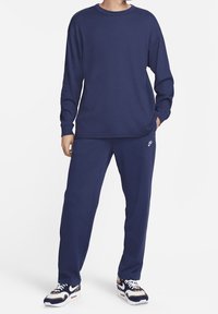 Námořnicky modré tričko s dlouhým rukávem a tepláky vyrobené z texturované látky, s malým logem Nike na kalhotách, nošené s vzorovanými teniskami.