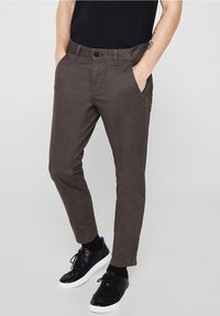 Tummanruskeat chinot slim fit -leikkauksella, joissa on sivutaskut, vyölenkit ja napitus vyötäröllä. Yhdistetty mustiin urheilukenkiin.