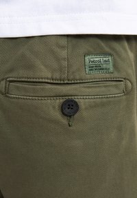 Groene katoenen twill stof met een gestructureerde oppervlakte. Kenmerkt een achterzak met een zwarte knop en een zichtbaar label met de tekst "Petrol Ind."
