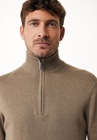 Maglione beige con collo alto e zip, realizzato in un tessuto lavorato a maglia. Il materiale sembra morbido e comodo.