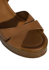 Braune Leder-Sandale mit überkreuzten Riemen und einer Plattformsohle. Sanfte Textur, abgerundete Spitze und sichtbare Nahtdetails.