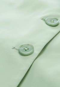 Hellgrüner Stoff mit zwei transparenten Knöpfen. Die Knöpfe haben ein Vierlochdesign mit passendem Faden. Glatte Textur, einfaches Design.