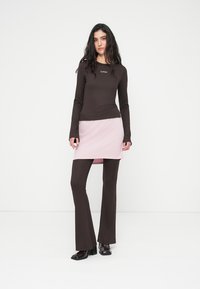 Καφέ τοπ με μακριά μανίκια και ροζ φούστα φορεμένα πάνω από καφέ φαρδιά παντελόνια. Λείο ύφασμα με ελάχιστη σήμανση στο τοπ. Λιτές μαύρες γυαλιστερές μπότες.