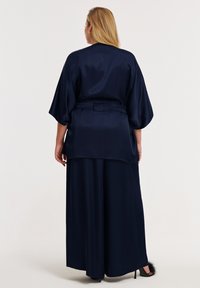 Ensemble en satin bleu marine comprenant un haut style kimono à larges manches, une taille ceinturée, et un pantalon à jambes larges avec des accents en fourrure noire douce à l'ourlet.