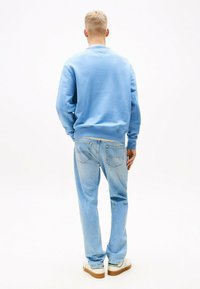 Sudadera azul claro con cuello redondo, fabricada en material sostenible y con puños de canalé. Combinada con jeans azul claro y zapatillas blancas.
