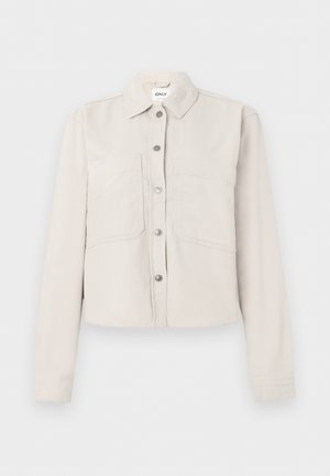 Svetlobéžová krátka bunda s dlhými rukávmi, striebornými patentkami vpredu, špicatým golierom a dvoma náprsnými vreckami.