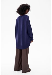 Marineblauwe oversized gebreide trui met ribboorden bij de mouwen en onderkant. Gecombineerd met bruine wijde broek. Soepele textuur, casual ontwerp.