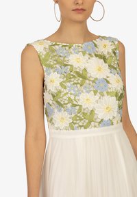 Bodice brodé avec des motifs floraux en blanc, vert et bleu ; jupe plissée blanche. Dispose d'un col bateau et d'un design sans manches.
