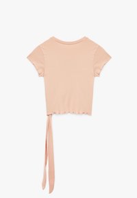 Camiseta corta de manga corta en rosa pastel, hecha de una tela suave, con un detalle de lazo en la parte posterior y un dobladillo con forma de ondas.