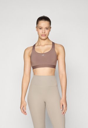 Brown sports bra with thick straps and a ribbed band. Pair of high-waisted beige leggings with subtle ribbing texture.