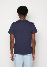 T-shirt de algodão azul-marinho com mangas curtas e decote redondo, vista pela parte de trás. Textura suave, design ajustado.
