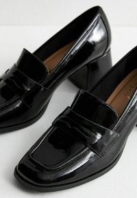 Black patent leather loafers with a square toe, low block heel, and decorative stitched detail on the upper. Smooth, glossy finish.