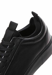 Sneaker in pelle nera con finitura liscia, caratterizzato da una punta arrotondata, lacci testurizzati e un inserto sul tallone rinforzato per una facile calzata.