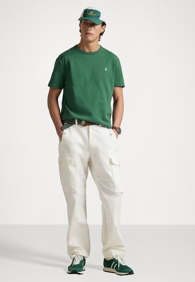 Grön bomulls t-shirt, vita cargo-byxor och gröna sneakers. Vit och grön keps med logotypaccent. Avslappnad och bekväm passform.