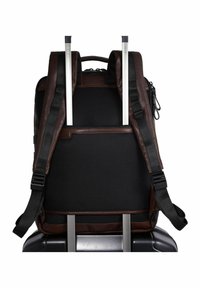 Brauner Leder- und schwarzer Netz-Rucksack mit verstellbaren Trägern, ausgestattet mit einem oberen Handgriff und einer Reißverschlusstasche, die auf einem Trolley-Griff liegt.