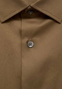 Tessuto della camicia marrone con una texture liscia, caratterizzato da un colletto classico e un bottone rotondo argentato. Cuciture visibili attorno al bordo del colletto.