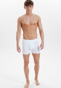 Weiße Baumwoll-Boxershorts mit einem weichen Bund, engem Schnitt und glatter Textur, präsentiert an einem männlichen Modell in einer neutralen Umgebung.