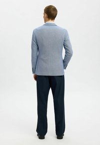 Veste de costume bleu clair au design ajusté avec des revers en pointe. Associée à un pantalon marine foncé. Tissu lisse avec une texture subtile.
