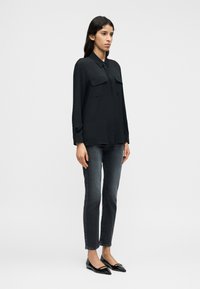 Μαύρο πουκάμισο με μακριά μανίκια και δύο τσέπες στο στήθος, συνδυασμένο με σκούρα, στενά τζιν και μαύρες μπαλαρίνες με μυτερή μύτη. Λείο ύφασμα.