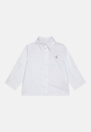 Camisa blanca de manga larga con botones, cuello puntiagudo y pequeño logotipo "CK" bordado en el pecho izquierdo.