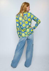 Blaues Langarmhemd mit einem sechseckigen Muster in Grün und Gelb, kombiniert mit hellblauen, lockeren Jeans mit Cargo-Taschen.