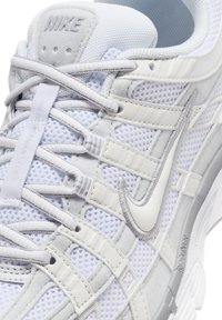 Gros plan d'une basket blanche Nike en tissu mesh, avec des accents gris, des lacets croisés et un logo Nike swoosh argenté bien visible sur le côté.