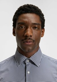 Tummansininen ja valkoinen ruutuplaid-paita, jossa on terävä kauluskanta ja nappisuljenta. Paidassa on keskipainoinen kangas ja sileä rakenne.