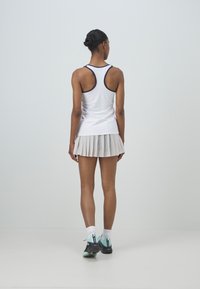 Top atlético blanco sin mangas con ribetes en azul marino, combinado con una falda blanca plisada que presenta textura de malla y zapatillas deportivas negras.