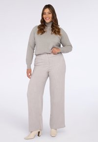 Vaalean harmaa pooloneule yhdistettynä vaalean harmaisiin väljiksi leikattuihin housuihin; sileä kangas, jossa on hieno tekstuuri; vaaleat korokepohjaiset kengät.