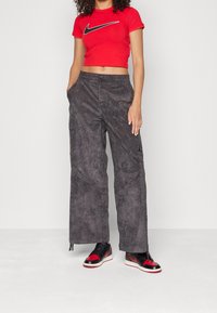 Czerwona krótka koszulka Nike z czarnym logo Swoosh, zestawiona z szarymi spodniami typu cargo o miękkiej fakturze i bocznych kieszeniach, dopełniona czarno-czerwonymi trampkami.