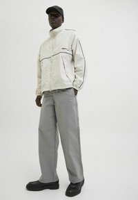 Jachetă ușoară albă cu accente negre, pantaloni gri largi și pantofi negri; modelul poartă de asemenea o șapcă neagră. Textură netedă pe toată suprafața.