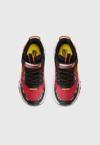 Black and red athletic shoes featuring a pixelated pattern, textured upper, yellow accents, and orange laces. Logo on the strap.