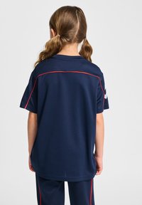 Marinblå träningsskjorta med korta ärmar, med röd accentstickning längs axlarna och ryggen. Texturerat tyg, avslappnad passform.