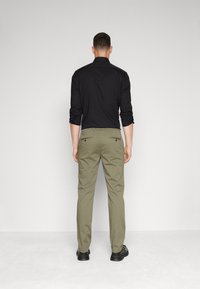 Camicia nera con bottoni, pantaloni khaki e scarpe nere. I pantaloni hanno tasche posteriori con bottoni e le maniche della camicia sono arrotolate.