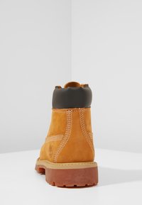 Stivaletto in suede marrone con suola beige, punta rotonda e colletto imbottito nero, caratterizzato da cuciture bianche e un logo sul lato.
