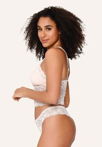 Set di lingerie in pizzo di un morbido colore crema, composto da un bralette con bordi ondulati e tanga coordinato, che mostrano delicati motivi floreali e una texture morbida.