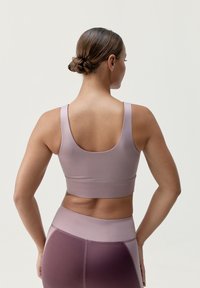 Fialová sportovní podprsenka s bezšvovým designem, širokými ramínky a těsným střihem. Hladká, pružná látka s jemným leskem a kontrastními akcenty.