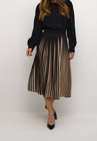 Plisserad kjol i beige och svart, med vertikala ränder och ett mjukt, flödande tyg. Kombinerad med en svart topp och spetsiga svarta klackar.