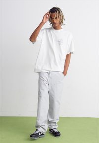 White cotton t-shirt with a front graphic, paired with light grey cargo pants. Black and white sneakers with distinctive design details.