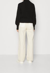 Maglione nero a coste con collo alto, abbinato a pantaloni larghi crema con tasche a pattina bianche e sneakers bianche.
