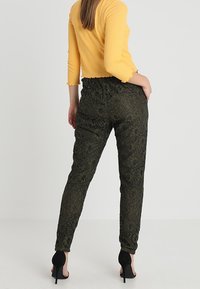 Czarne spodnie w kwiatowy wzór z elastycznym pasem i zwężanymi nogawkami, zestawione z fakturowanym żółtym topem i czarnymi szpilkami.