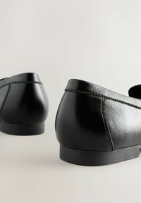 Kaks paari musta nahast loafers-kingi, sileda viimistluse, ümarate varvastega, minimaalse õmblusega ja lameda kummist tallaga.